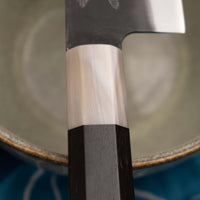 Yoshida Gyuto SUJ-2 Kuro-uchi 210 mm je ročno izdelan srednje velik kuhinjski nož, popoln za različna opravila v kuhinji. Kuro-uchi serija Yoshida Hamono združuje trpežno SUJ-2 jeklo (64,7 HRC) za izjemno obstojnost ostrine in kuro-uchi zaključek, ki zagotavlja rustikalen videz in dodatno zaščito rezila. Ročaj iz ebenovine omogoča varen oprijem in natančen nadzor pri rezanju.