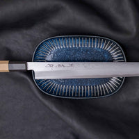 Kawamura Kiritsuke Yanagiba predstavlja vrh japonske umetnosti kovanja nožev. Izvira iz enega najslavnejših nožarskih središč dežele vzhajajočega sonca, kjer so ga ročno skovali mojstri kovačije Sakai Kikumori. Rezilo krasi damask vzorec, ki se preko kireha linije zliva skoraj vse do rezalnega roba.