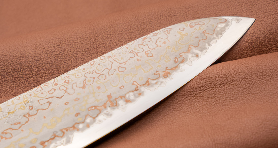Hayabusa Gyuto Aogami #2 Rainbow Damascus 210 mm je nož za vsestransko uporabo v kuhinji, primeren za meso, ribe in zelenjavo. Tanko rezilo je narejeno iz Aogami #2 jekla, znanega po dolgem ohranjanju ostrine in lahkosti brušenja. Ima unikaten barvit damaščanski vzorec, izdelan s plastenjem medenine in bakra.