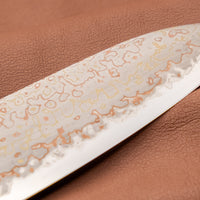 Hayabusa Gyuto Aogami #2 Rainbow Damascus 210 mm je nož za vsestransko uporabo v kuhinji, primeren za meso, ribe in zelenjavo. Tanko rezilo je narejeno iz Aogami #2 jekla, znanega po dolgem ohranjanju ostrine in lahkosti brušenja. Ima unikaten barvit damaščanski vzorec, izdelan s plastenjem medenine in bakra.