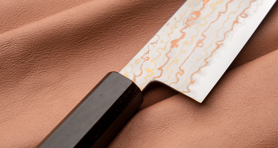 Hayabusa Gyuto Aogami #2 Rainbow Damascus 210 mm je nož za vsestransko uporabo v kuhinji, primeren za meso, ribe in zelenjavo. Tanko rezilo je narejeno iz Aogami #2 jekla, znanega po dolgem ohranjanju ostrine in lahkosti brušenja. Ima unikaten barvit damaščanski vzorec, izdelan s plastenjem medenine in bakra.