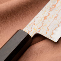 Hayabusa Gyuto Aogami #2 Rainbow Damascus 210 mm je nož za vsestransko uporabo v kuhinji, primeren za meso, ribe in zelenjavo. Tanko rezilo je narejeno iz Aogami #2 jekla, znanega po dolgem ohranjanju ostrine in lahkosti brušenja. Ima unikaten barvit damaščanski vzorec, izdelan s plastenjem medenine in bakra.