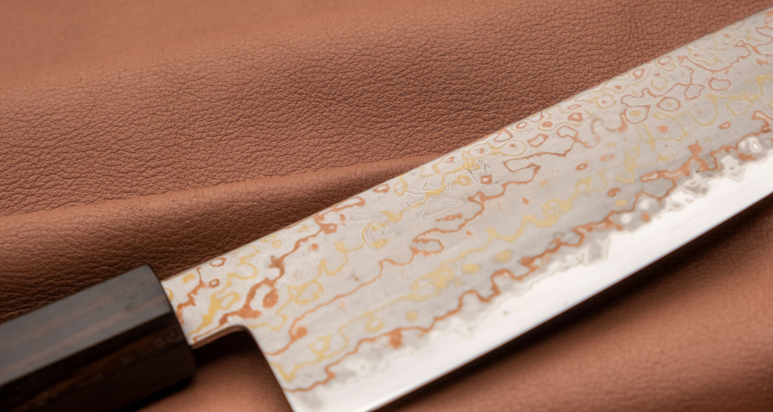 Hayabusa Gyuto Aogami #2 Rainbow Damascus 210 mm je nož za vsestransko uporabo v kuhinji, primeren za meso, ribe in zelenjavo. Tanko rezilo je narejeno iz Aogami #2 jekla, znanega po dolgem ohranjanju ostrine in lahkosti brušenja. Ima unikaten barvit damaščanski vzorec, izdelan s plastenjem medenine in bakra.