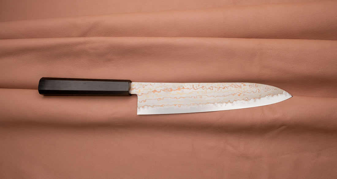 Hayabusa Gyuto Aogami #2 Rainbow Damascus 210 mm je nož za vsestransko uporabo v kuhinji, primeren za meso, ribe in zelenjavo. Tanko rezilo je narejeno iz Aogami #2 jekla, znanega po dolgem ohranjanju ostrine in lahkosti brušenja. Ima unikaten barvit damaščanski vzorec, izdelan s plastenjem medenine in bakra.