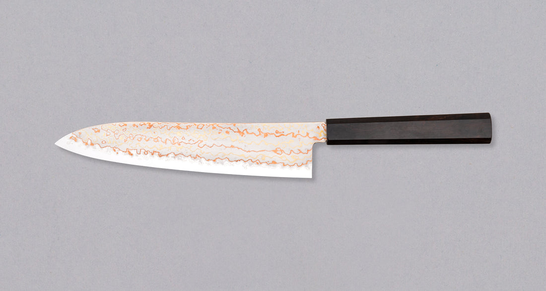 Hayabusa Gyuto Aogami #2 Rainbow Damascus 210 mm je nož za vsestransko uporabo v kuhinji, primeren za meso, ribe in zelenjavo. Tanko rezilo je narejeno iz Aogami #2 jekla, znanega po dolgem ohranjanju ostrine in lahkosti brušenja. Ima unikaten barvit damaščanski vzorec, izdelan s plastenjem medenine in bakra.