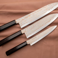 Hayabusa Gyuto Aogami #2 Rainbow Damascus 210 mm je nož za vsestransko uporabo v kuhinji, primeren za meso, ribe in zelenjavo. Tanko rezilo je narejeno iz Aogami #2 jekla, znanega po dolgem ohranjanju ostrine in lahkosti brušenja. Ima unikaten barvit damaščanski vzorec, izdelan s plastenjem medenine in bakra.