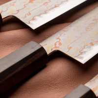 Hayabusa Gyuto Aogami #2 Rainbow Damascus 210 mm je nož za vsestransko uporabo v kuhinji, primeren za meso, ribe in zelenjavo. Tanko rezilo je narejeno iz Aogami #2 jekla, znanega po dolgem ohranjanju ostrine in lahkosti brušenja. Ima unikaten barvit damaščanski vzorec, izdelan s plastenjem medenine in bakra.