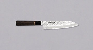 Kawamura Santoku Damascus je vsestranski japonski kuhinjski nož, ročno kovan in laminiran po metodi san-mai. Sredica je izdelana iz jekla AUS-10 in ovita v plasti damaščanskega jekla, zgornji del pa rezila krasijo odtisi kladiva. Japonski ročaj je izdelan iz žganega kostanjevega lesa z obročkom iz bivoljega roga.
