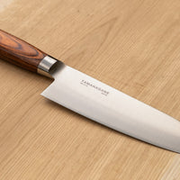 Tamahagane "SAN" Santoku 160 mm - Rezilo je kovano iz jekla VG-5 z visokim odstotkom ogljika, molibdenom in vanadijem ter z izjemno trdoto 61 HRC, rezalni rob je ročno brušen pod kotom med 14 in 15˚. Nož združuje popolno uravnoteženost med ostrino in trdnostjo, zato je primerno tudi za profesionalno delovno okolje.