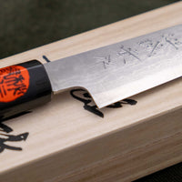Tanaka Petty Aogami #2 Damascus 150mm je odlična izbira za vse kuharje, ki želijo ročno kovan japonski nož iz tradicionalnega jekla s pravo japonsko fino ostrino. Nož z minimalističnim zaključnim videzom na rezilu in klasičnim wa ročajem iz lesa magnolije pooseblja japonsko estetiko. Pride v paulownia leseni škatlici.