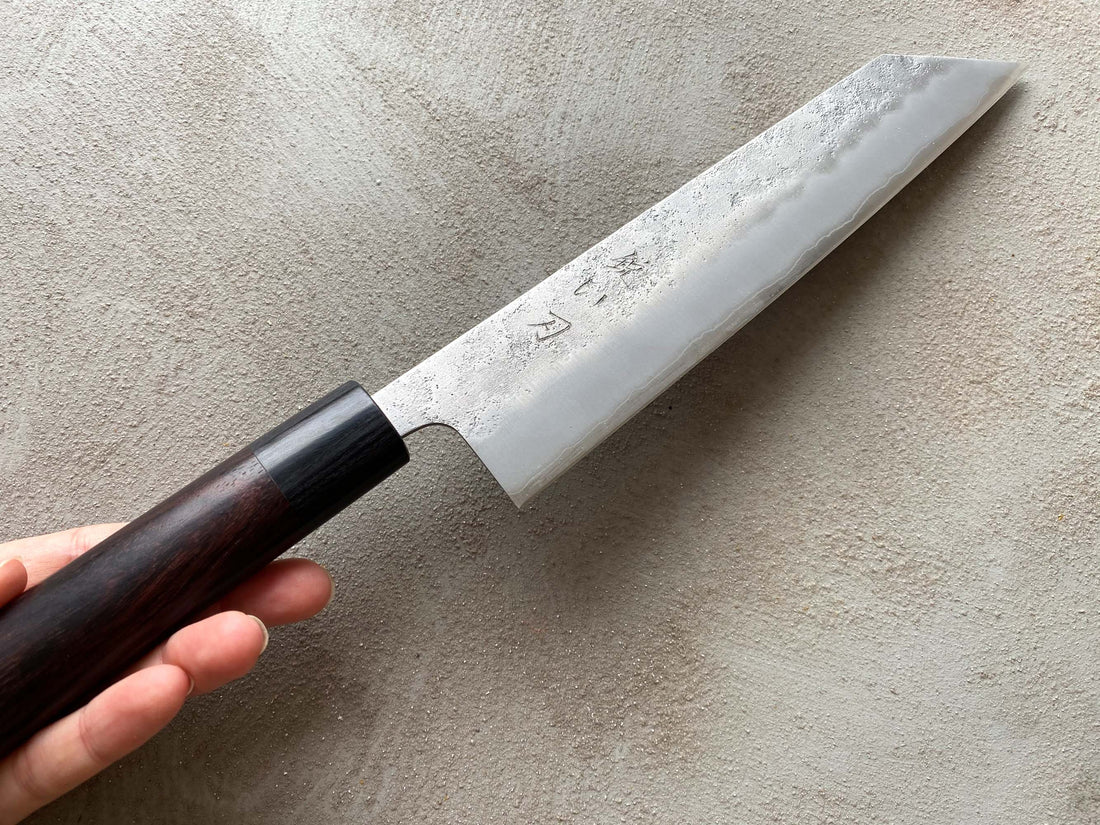 Hokiyama Kiritsuke Ginsanko Rosewood 210 mm_4  Čeprav je profil rezila Hokiyama Kiritsuke Ginsanko Rosewood nekoliko bolj raven kot pri Gyuto nožih, gre še vedno za večnamenski nož, primeren za vsakodnevno uporabo, saj je dolžina rezila 210 mm optimalna velikost za sekljanje zelenjave ter rezanje večjih kosov mesa in rib. Nož zaznamujejo odtisi kladiva nashiji.