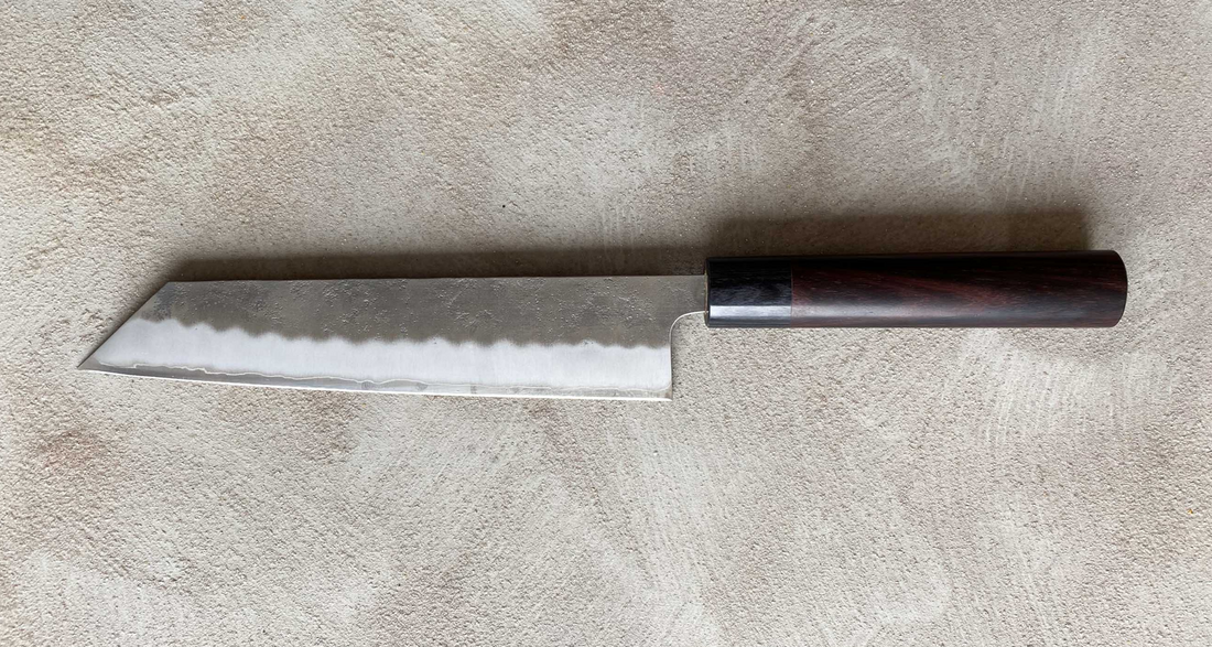Hokiyama Kiritsuke Ginsanko Rosewood 210 mm_2  Čeprav je profil rezila Hokiyama Kiritsuke Ginsanko Rosewood nekoliko bolj raven kot pri Gyuto nožih, gre še vedno za večnamenski nož, primeren za vsakodnevno uporabo, saj je dolžina rezila 210 mm optimalna velikost za sekljanje zelenjave ter rezanje večjih kosov mesa in rib. Nož zaznamujejo odtisi kladiva nashiji.