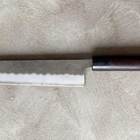 Hokiyama Kiritsuke Ginsanko Rosewood 210 mm_2 Čeprav je profil rezila Hokiyama Kiritsuke Ginsanko Rosewood nekoliko bolj raven kot pri Gyuto nožih, gre še vedno za večnamenski nož, primeren za vsakodnevno uporabo, saj je dolžina rezila 210 mm optimalna velikost za sekljanje zelenjave ter rezanje večjih kosov mesa in rib. Nož zaznamujejo odtisi kladiva nashiji.