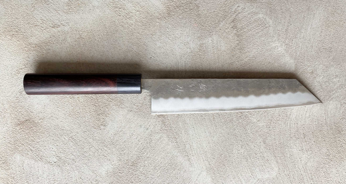 Hokiyama Kiritsuke Ginsanko Rosewood 210 mm_3  Čeprav je profil rezila Hokiyama Kiritsuke Ginsanko Rosewood nekoliko bolj raven kot pri Gyuto nožih, gre še vedno za večnamenski nož, primeren za vsakodnevno uporabo, saj je dolžina rezila 210 mm optimalna velikost za sekljanje zelenjave ter rezanje večjih kosov mesa in rib. Nož zaznamujejo odtisi kladiva nashiji.