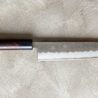 Hokiyama Kiritsuke Ginsanko Rosewood 210 mm_3 Čeprav je profil rezila Hokiyama Kiritsuke Ginsanko Rosewood nekoliko bolj raven kot pri Gyuto nožih, gre še vedno za večnamenski nož, primeren za vsakodnevno uporabo, saj je dolžina rezila 210 mm optimalna velikost za sekljanje zelenjave ter rezanje večjih kosov mesa in rib. Nož zaznamujejo odtisi kladiva nashiji.