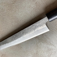 Hokiyama Kiritsuke Ginsanko Rosewood 210 mm_5 Čeprav je profil rezila Hokiyama Kiritsuke Ginsanko Rosewood nekoliko bolj raven kot pri Gyuto nožih, gre še vedno za večnamenski nož, primeren za vsakodnevno uporabo, saj je dolžina rezila 210 mm optimalna velikost za sekljanje zelenjave ter rezanje večjih kosov mesa in rib. Nož zaznamujejo odtisi kladiva nashiji.