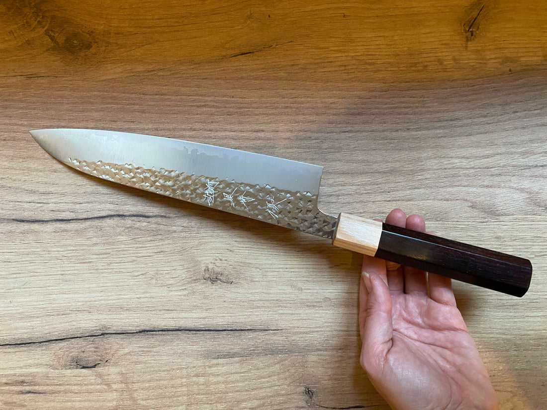 Kurosaki Gyuto Senko R2 210 mm_3 Kurosaki Gyuto iz linije Senko je še eno unikatno rezilo iz rok nadarjenega mladega kovaškega mojstra Yu Kurosakija. Edinstveni odtisi kladiva na zgornjem delu rezila spominjajo na bleščeč diamantni vzorec – od tod tudi ime senko. Rezilo je obdelano do videza visokega sijaja, ki je v čudovitem kontrastu s temnim lesenim ročajem.