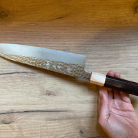 Kurosaki Gyuto Senko R2 210 mm_3 Kurosaki Gyuto iz linije Senko je še eno unikatno rezilo iz rok nadarjenega mladega kovaškega mojstra Yu Kurosakija. Edinstveni odtisi kladiva na zgornjem delu rezila spominjajo na bleščeč diamantni vzorec – od tod tudi ime senko. Rezilo je obdelano do videza visokega sijaja, ki je v čudovitem kontrastu s temnim lesenim ročajem.