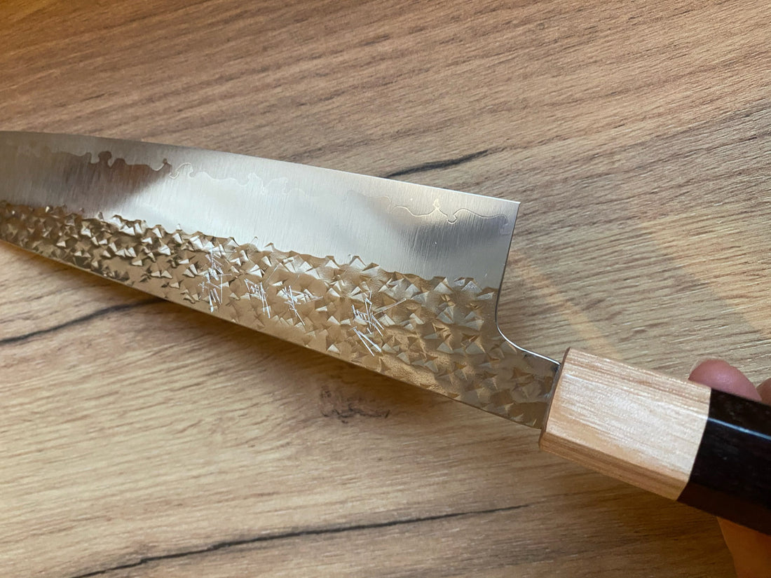 Kurosaki Gyuto Senko R2 210 mm_2 Kurosaki Gyuto iz linije Senko je še eno unikatno rezilo iz rok nadarjenega mladega kovaškega mojstra Yu Kurosakija. Edinstveni odtisi kladiva na zgornjem delu rezila spominjajo na bleščeč diamantni vzorec – od tod tudi ime senko. Rezilo je obdelano do videza visokega sijaja, ki je v čudovitem kontrastu s temnim lesenim ročajem.