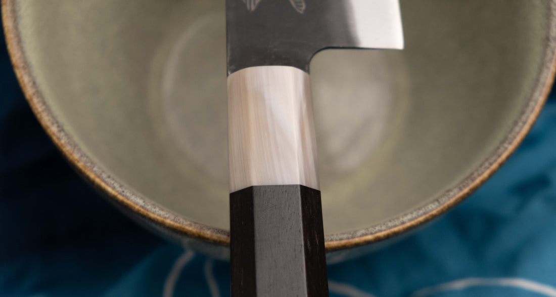 Yoshida Gyuto SUJ-2 Kuro-uchi 210 mm je ročno izdelan srednje velik kuhinjski nož, popoln za različna opravila v kuhinji. Kuro-uchi serija Yoshida Hamono združuje trpežno SUJ-2 jeklo (64,7 HRC) za izjemno obstojnost ostrine in kuro-uchi zaključek, ki zagotavlja rustikalen videz in dodatno zaščito rezila. Ročaj iz ebenovine omogoča varen oprijem in natančen nadzor pri rezanju. 