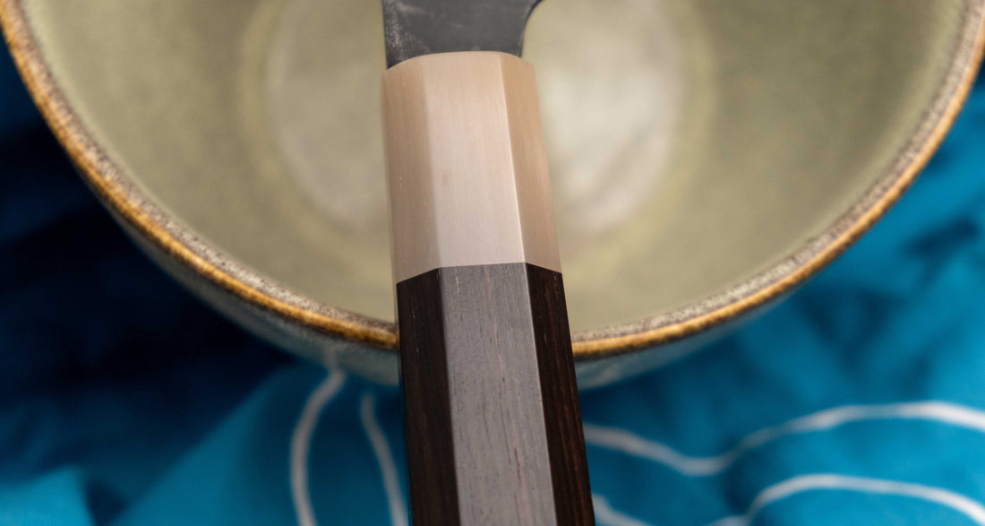 Yoshida Bunka SUJ-2 Kuro-uchi 190 mm ročno izdelan kuhinjski nož iz serije Yoshida Hamono, s trpežnim SUJ-2 jeklom, rustikalnim kuro-uchi zaključkom, ročajem iz ebenovine ter unikatno gravuro koi krapa, idealen za raznolika kuhinjska opravila in kot darilo.