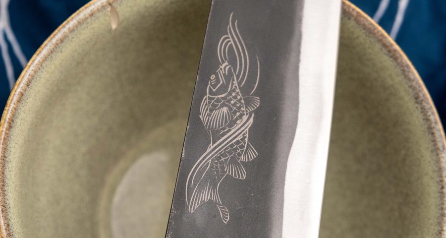 Yoshida Bunka SUJ-2 Kuro-uchi 190 mm ročno izdelan kuhinjski nož iz serije Yoshida Hamono, s trpežnim SUJ-2 jeklom, rustikalnim kuro-uchi zaključkom, ročajem iz ebenovine ter unikatno gravuro koi krapa, idealen za raznolika kuhinjska opravila in kot darilo.