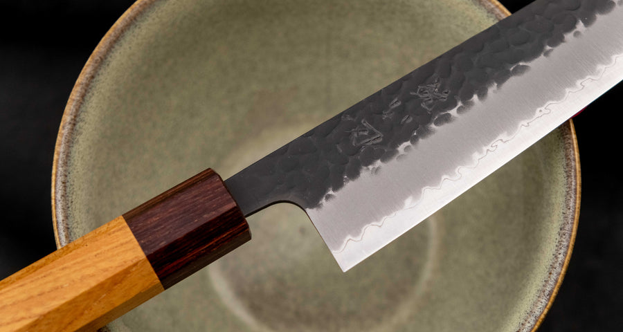 Japonski nož Hokiyama Bunka Aogami Super Kuro-uchi 170 mm je večnamenski nož iz Aogami Super jekla, ki dolgo časa drži ostrino. Kuro-uchi patina ga ščiti pred korozijo, odtisi kladiv pa preprečujejo lepljenje hrane na rezilo. Ima tradicionalni japonski wa ročaj oktagonalne oblike iz mahagonija in zelkovega lesa.