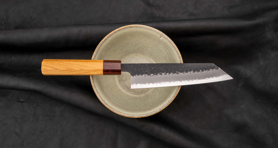 Japonski nož Hokiyama Bunka Aogami Super Kuro-uchi 170 mm je večnamenski nož iz Aogami Super jekla, ki dolgo časa drži ostrino. Kuro-uchi patina ga ščiti pred korozijo, odtisi kladiv pa preprečujejo lepljenje hrane na rezilo. Ima tradicionalni japonski wa ročaj oktagonalne oblike iz mahagonija in zelkovega lesa.