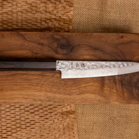 Hayabusa Petty VG-10 Tsuchime Damascus Ebony 150 mm je manjši vsestranski nož z vidnimi odtisi kladiv, elegantnim damask vzorcem in klasičnim japonskim ročajem (wa-style) iz lesa ebenovine. 