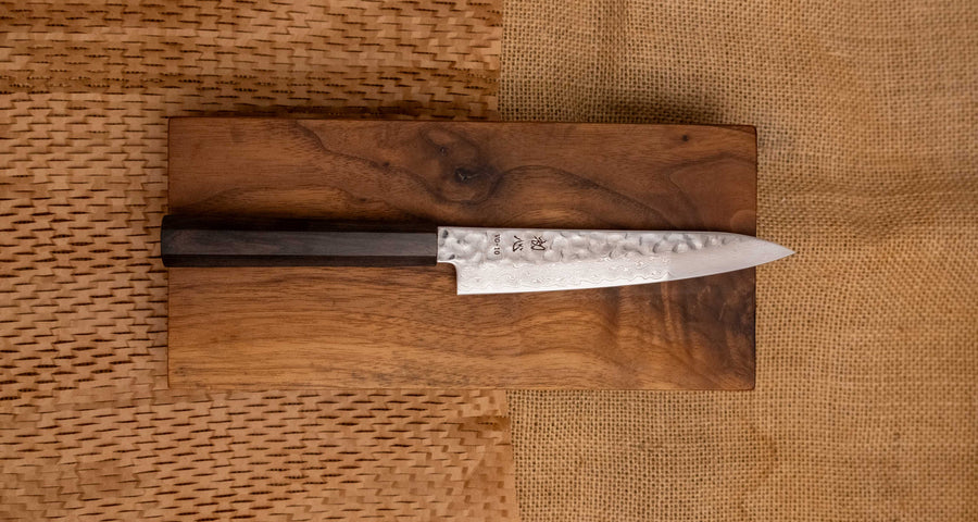 Hayabusa Petty VG-10 Tsuchime Damascus Ebony 150 mm je manjši vsestranski nož z vidnimi odtisi kladiv, elegantnim damask vzorcem in klasičnim japonskim ročajem (wa-style) iz lesa ebenovine. 