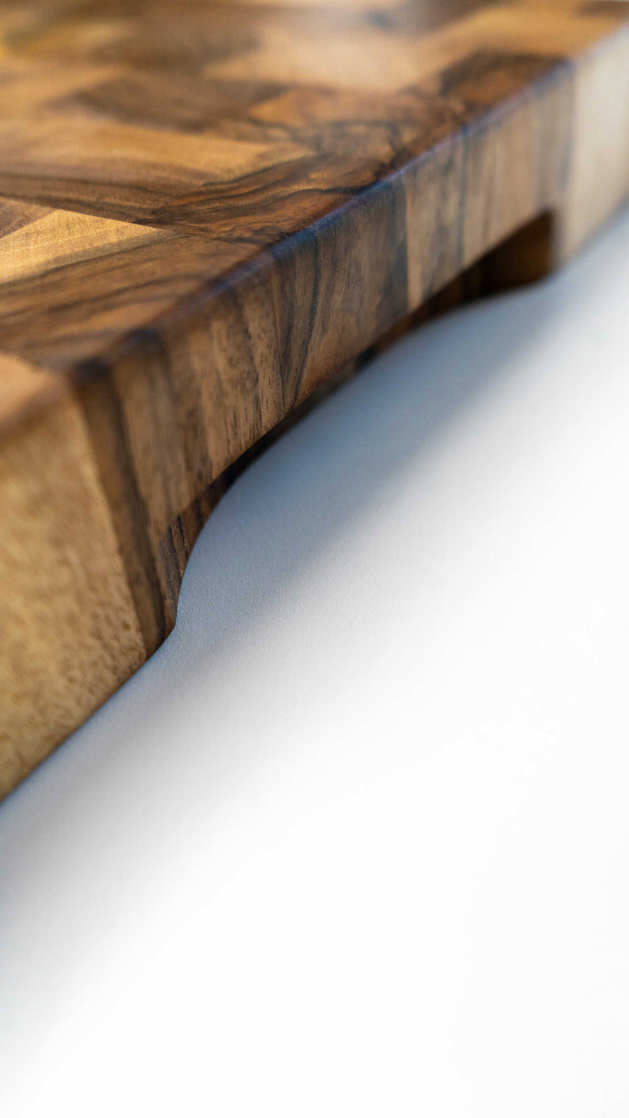 Ročno izdelana kuhinjska deska za rezanje je narejena iz orehovega lesa. Posebnost te deske je, da je sestavljena tako, da so vlakna lesa obrnjena navzgor in zato nudi boljše pogoje za rezanje, saj takšna podlaga manj poškoduje rezalno površino noža. V kompletu z desko je tudi olje za nego in zaščito lesenih površin. Na sliki: Rob rezalne deske, prilagojen za oprijem z dlanmi.