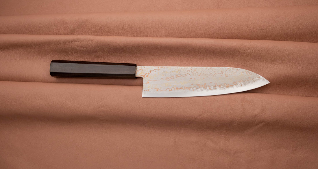 Hayabusa Santoku Aogami #2 Rainbow Damascus 180 mm je nož za vsestransko uporabo v kuhinji, primeren za meso, ribe in zelenjavo. Tanko rezilo je narejeno iz Aogami #2 jekla, znanega po dolgem ohranjanju ostrine in lahkosti brušenja. Ima unikaten barvit damaščanski vzorec, izdelan s plastenjem medenine in bakra.