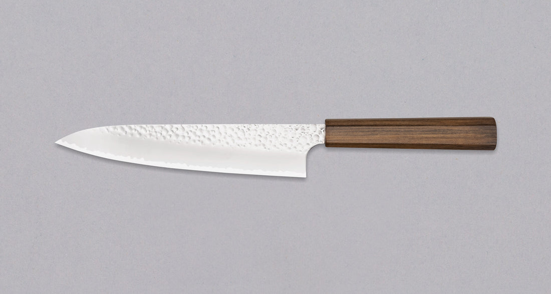 Hayabusa Gyuto VG-10 Tsuhime Bubinga 210 mm je vsestranski nož, ki je primeren za uporabo v domači in profesionalni kuhinji. Tanko in natančno rezilo iz vrhunskega VG-10 jekla omogoča enostavno delo tudi z drobnimi sestavinami. Nož izstopa s prefinjenim videzom: migaki rezilo krasi droben vzorec kladiva, medtem ko izrazita valovita linija ločuje plasti jekla in jedro, ustvarjajoč kontrast med matirano in sijočo površino.