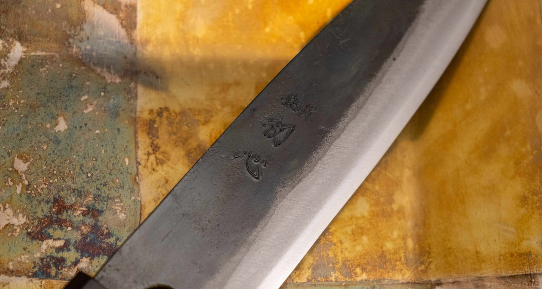 Detajl Kokugei Santoku Aogami #1 Kuro-uchi Ebony 165 mm, ki prikazuje kuro-uchi površinsko obdelavo rezila in kanji pismenke.