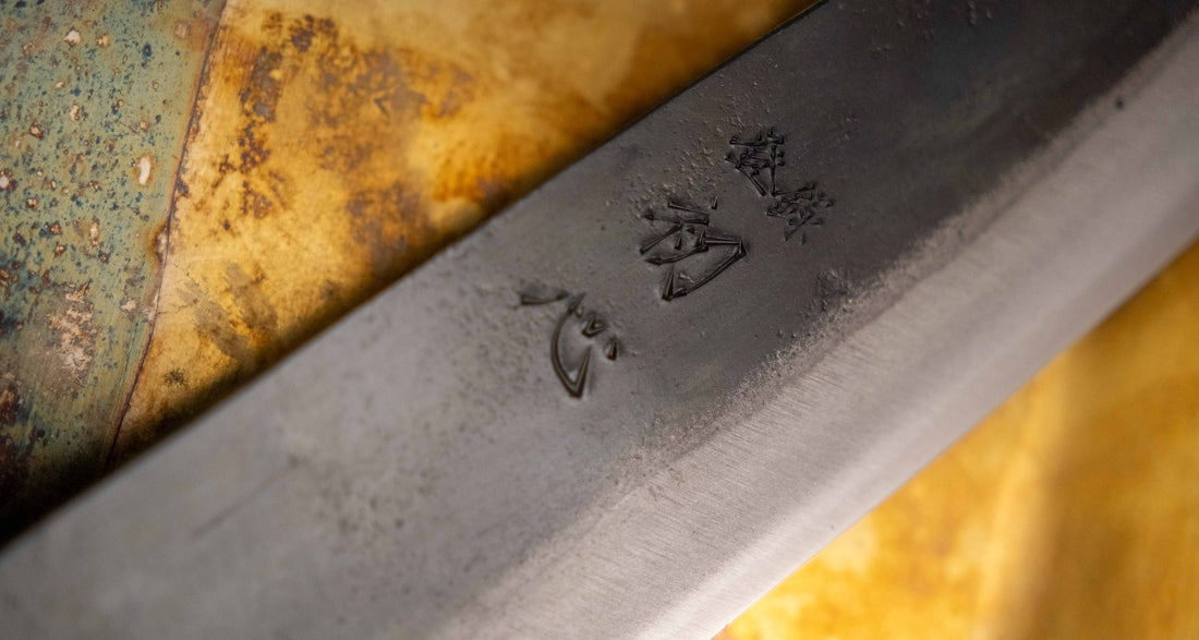Detajl Kokugei Santoku Aogami #1 Kuro-uchi Ebony 165 mm, ki prikazuje kuro-uchi površinsko obdelavo rezila in kanji pismenke.