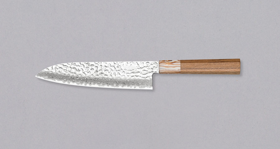 Kotetsu Santoku VG-10 Damascus 180 mm je velik vsestranski nož z vidnimi odtisi kladiv, damascus vzorcem in klasičnim japonskim ročajem (wa-style) iz tikovine. Je izjemno tanek (1,7 mm), zato bo zlahka zdrsel skozi sestavine, nerjaveče VG-10 jeklo pa zagotavlja odpornost na rjo, trpežnost in odpornost proti obrabi.