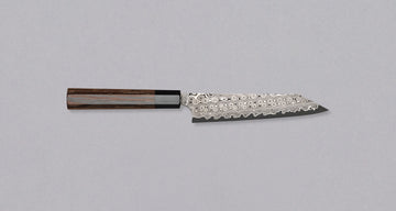 Nigara Kiritsuke Petty SG2 Damascus 150 mm je majhen japonski kuhinjski nož, primeren za delikatna in manjša rezalna opravila v dlani in na rezalni desk Jedro iz prašnega jekla SG2 ter hamaguri presek profila zagotavljata dolgotrajno ostrino ter minimalno vzdrževanje. Nož krasi poseben vzorec dežnih kapljic - amatsubu.
