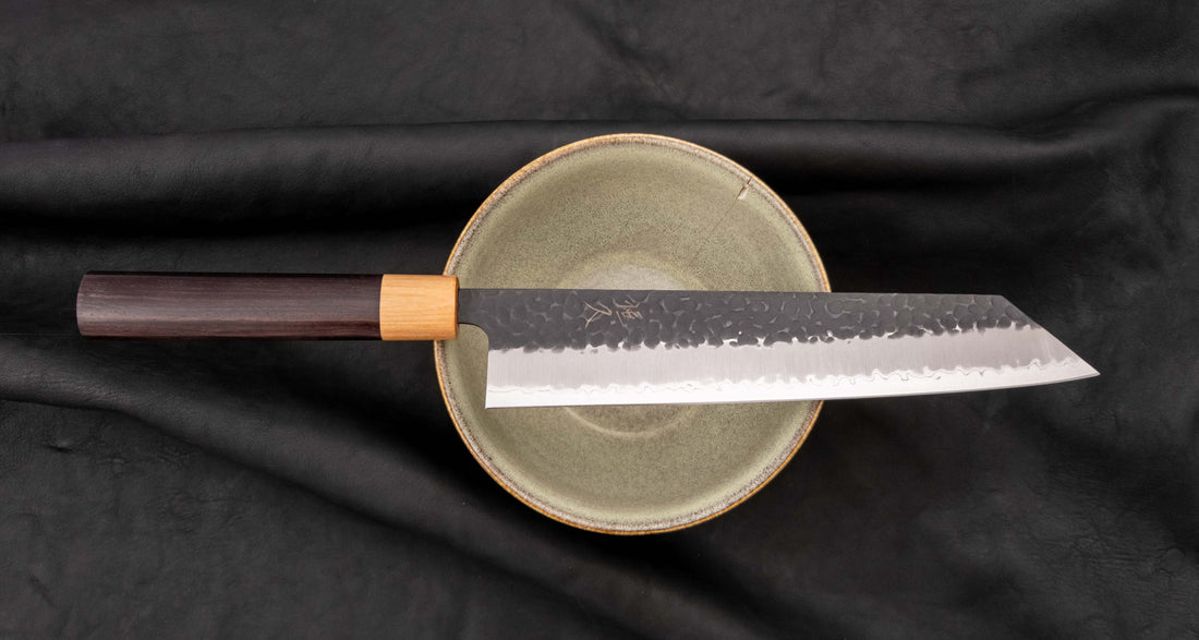 Tsunehisa Kiritsuke AS Kuro-uchi 240 mm je japonski nož, ki ga poleg enega najboljših jekel za kuhinjske nože in popolnega profila rezila (zelo tanko rezilo!), zaznamuje tudi unikatna kombinacija temne patine in odtisov kladiva, ki ju vizualno lepo dopolnjuje klasičen japonski ročaj iz palisandra in javorjevega lesa.