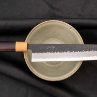 Tsunehisa Kiritsuke AS Kuro-uchi 240 mm je japonski nož, ki ga poleg enega najboljših jekel za kuhinjske nože in popolnega profila rezila (zelo tanko rezilo!), zaznamuje tudi unikatna kombinacija temne patine in odtisov kladiva, ki ju vizualno lepo dopolnjuje klasičen japonski ročaj iz palisandra in javorjevega lesa.