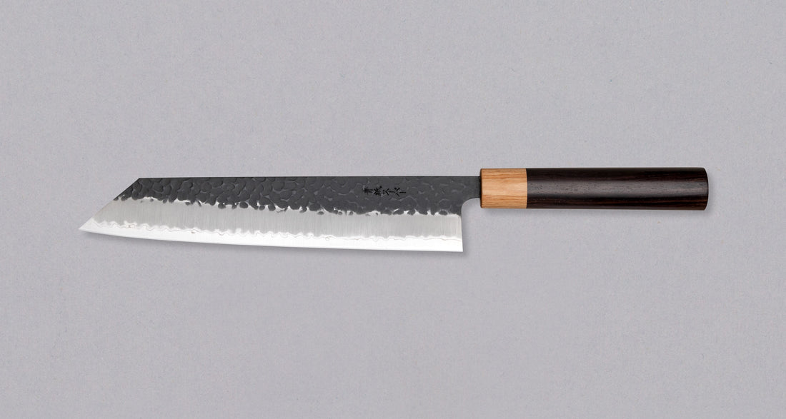 Tsunehisa Kiritsuke AS Kuro-uchi 240 mm je japonski nož, ki ga poleg enega najboljših jekel za kuhinjske nože in popolnega profila rezila (zelo tanko rezilo!), zaznamuje tudi unikatna kombinacija temne patine in odtisov kladiva, ki ju vizualno lepo dopolnjuje klasičen japonski ročaj iz palisandra in javorjevega lesa.