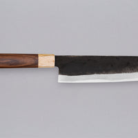 Yoshida Nakiri Kyusyu SUJ-2 Kuro-uchi 165 mm [Rosewood-Cedar] je tradicionalen japonski nož za rezanje zelenjave. Sredica noža je izdelana iz SUJ-2 jekla, rezilo pa je opremljeno s tradicionalnim japonskim ročajem iz palisandra, ki na vrhu prehaja v zaključni obroček iz lesa cedre.