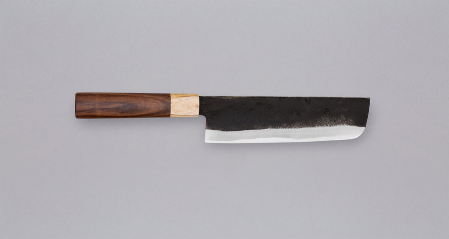 Yoshida Nakiri Kyusyu SUJ-2 Kuro-uchi 165 mm [Rosewood-Cedar] je tradicionalen japonski nož za rezanje zelenjave. Sredica noža je izdelana iz SUJ-2 jekla, rezilo pa je opremljeno s tradicionalnim japonskim ročajem iz palisandra, ki na vrhu prehaja v zaključni obroček iz lesa cedre.