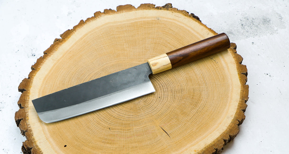 Yoshida Nakiri Kyusyu SUJ-2 Kuro-uchi 165 mm [Rosewood-Cedar] je tradicionalen japonski nož za rezanje zelenjave. Sredica noža je izdelana iz SUJ-2 jekla, rezilo pa je opremljeno s tradicionalnim japonskim ročajem iz palisandra, ki na vrhu prehaja v zaključni obroček iz lesa cedre.