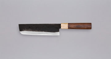 Yoshida Nakiri Kyusyu SUJ-2 Kuro-uchi 165 mm [Rosewood-Cedar] je tradicionalen japonski nož za rezanje zelenjave. Sredica noža je izdelana iz SUJ-2 jekla, rezilo pa je opremljeno s tradicionalnim japonskim ročajem iz palisandra, ki na vrhu prehaja v zaključni obroček iz lesa cedre.